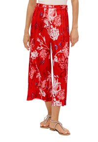 Pantaloni larghi e corti rossi con stampa floreale in rosa e blu, vita elastica con cordoncino, indossati con sandali piatti argentati con fasce.