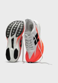 Zapatillas de running en blanco, negro y naranja neón. Parte superior de malla ligera, suela de goma texturizada con tacos triangulares para tracción.