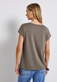 T-shirt olive court à manches courtes avec une coupe décontractée et un ourlet arrondi, fabriqué à partir d'un tissu doux. Porté avec un jean en denim bleu clair.