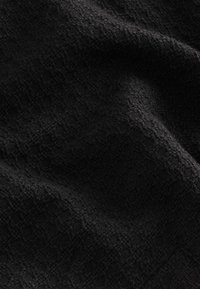 Melna teksturēta auduma ar austu rakstu, kas izceļ mīkstu, nedaudz raupju virsmu un bagātu, tumšu toni.