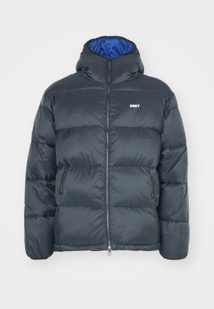 Pufferjacke in Schwarz mit Reißverschluss, Kapuze und blauen Futter. Verfügt über ein kleines weißes Logo auf der Brust und seitliche Taschen.
