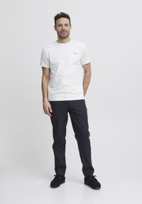 White cotton t-shirt with short sleeves features three small colored dots on the chest; paired with dark navy pants and black shoes.
