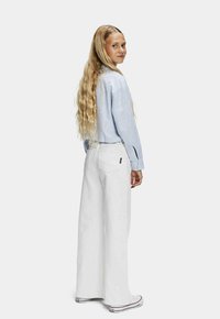 Gestreepte lichtblauwe overhemd met knopen, witte wijde broek en witte sneakers. Lang, golvend haar. Eenvoudig ontwerp en schone kleuren.