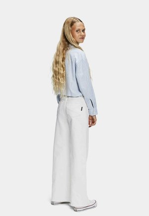 Gestreifte hellblaue Hemdbluse, weiße weite Hose und weiße Turnschuhe. Lange, wellige Haare. Einfaches Design und klare Farben.