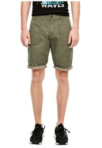 Shorts cargo verts olive avec des ourlets retroussés, poches avant, fermeture à bouton, fabriqués en tissu léger. Assortis à des chaussures de sport noires.