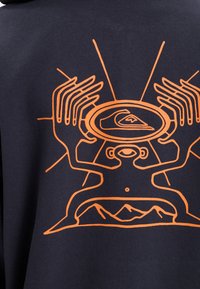Navy sweatshirt featuring an orange graphic design of hands and a person with a mountain backdrop, highlighting intricate line work.