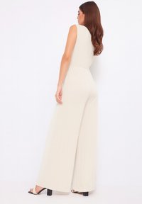 Completo beige senza maniche con vita aderente e design a gamba larga. Tessuto morbido e stile minimalista. Sandali neri con tacco completano il look.