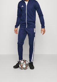 Marine trainingsjack en broek met witte strepen, gemaakt van glad sportmateriaal. Zwarte voetbal met sterpatroon.