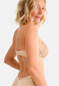 Reggiseno beige con ricami floreali, spalline regolabili e una fascia liscia. Il design presenta una texture delicata e una forma triangolare classica.