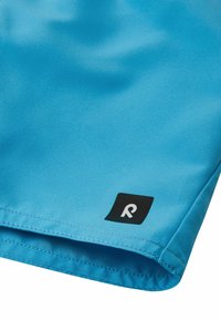 Jasnoniebieskie szorty z gładkiego materiału, z haftowanym wykończeniem, z małą czarną metką z logo w rogu.