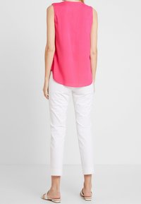 Top sans manches rose vif avec un ourlet arrondi, associé à un pantalon blanc court et des sandales plates avec une semelle rayée.