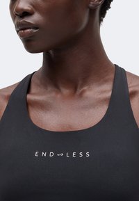 Gros plan d'une personne portant un haut noir sans manches avec le mot "ENDLESS" imprimé en blanc sur la poitrine.