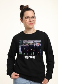 Felpa nera con stampa grafica che raffigura un gruppo di uomini in giacca e cravatta da "I Soprano," con testo bianco sotto l'immagine che dice "I Soprano."