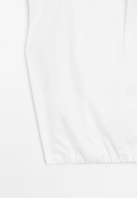 White garment with a smooth texture, featuring a gathered elastic hem. Simple design with no visible patterns or hardware accents.