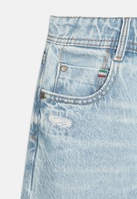 Tessuto in denim azzurro chiaro con una finitura sbiadita. Presenta una piccola area di usura, un bottone metallico e cuciture decorative in rosso, bianco e verde.