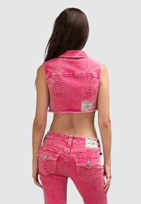 Wycierany różowy denimowy krótki kamizelka oraz pasujące dżinsy, z metalowymi akcentami, dwiema tylnymi kieszeniami oraz etykietami materiałowymi na pasku.