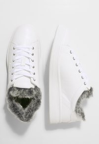 Bílé tenisky s hladkým koženým svrškem, šněrováním a šedou umělou kožešinou uvnitř. Mají gumovou podešev a minimální značení.