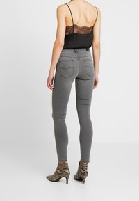 Vaqueros pitillo grises de tiro alto, con bolsillos traseros y detalles de costuras. La modelo lleva una camiseta negra con encaje y botines estampados.