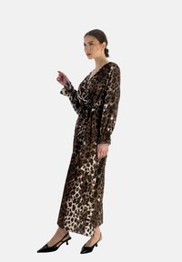 Robe maxi à imprimé léopard en brun et crème, avec des manches longues, un design enroulé et une taille nouée. Des chaussures à talons noires complètent la tenue.