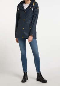 Veste imperméable marine avec capuche, accents dorés et boutons-pression jaunes. Comprend deux poches avant et une taille cintrée réglable.