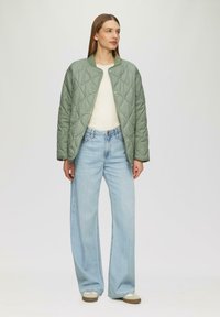 Quilted grüner Bomberjacke, cremiges Oberteil, hellblaue weit geschnittene Jeans und beiges Schuhwerk. Die Jacke hat Druckknöpfe und einen gerippten Kragen.