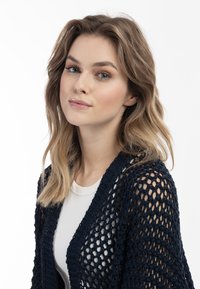 Cardigan all'uncinetto blu navy con design a maglia aperta, caratterizzato da scollatura a V e una vestibilità rilassata. Indossato sopra una maglietta di colore chiaro.