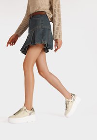 Gonna in denim a campana con orlo grezzo abbinata a chunky sneakers bianche con piattaforma e dettagli metallici, con lacci.