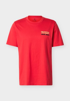 Rood T-shirt met korte mouwen en ronde hals, met kleine gele tekst "THE COURT HAS A NEW SHERIFF" en een zwarte strook met sterren op de bovenste linkerborst.