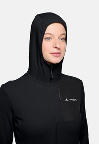 Giacca nera con zip e cappuccio aderente, realizzata in tessuto liscio. Presenta una tasca con zip sul petto e un dettaglio con logo sulla parte anteriore.