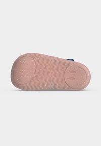 Semelle de chaussure rose mouchetée avec une bulle de dialogue embossée au talon et un visage souriant près des orteils, posée sur un fond blanc uni.