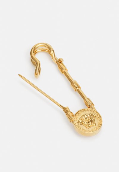 Gold safety pin-shaped earring with a lion head medallion detail. Features twisted wire accents and a smooth, reflective surface.