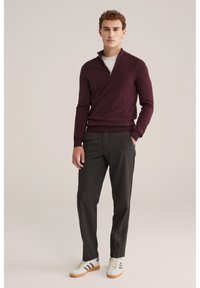 Burgundski pulover na zadrgo, slim fit, v kombinaciji s temno sivimi hlačami in belimi supergami z rjavimi detajli. Gladka tekstura, sproščen dizajn.