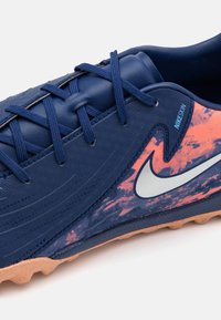 Marineblauwe voetbalschoen gemaakt van Nikeskin-materiaal, met een gestructureerd oppervlak, oranje-gradiëntaccenten en een lichtbruine rubberen zool.