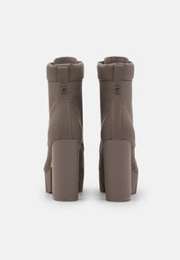 Bottines synthétiques marron à texture lisse, dotées de talons épais, de fermetures éclair latérales et de détails subtils de coutures.