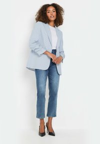 Ljust blå rutmönstrad kavaj med skräddarsydd passform, vit t-shirt under, kombinerad med ljusblå jeans och svarta högklackade skor.