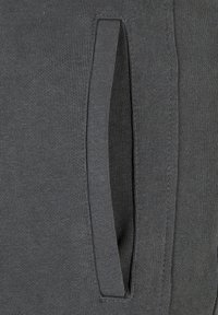 Material tricotat gri cu buzunar lateral și textură nervurată. Detaliile cusăturii de lângă buzunar sporesc structura și designul.