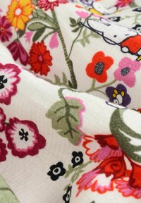 Tissu floral présentant une variété de fleurs aux couleurs vives, principalement en rouge, rose et orange, sur un fond blanc léger et texturé.