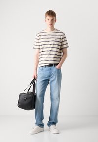 Tricou cu mânecă scurtă în dungi, crem și bleumarin, blugi deschiși la culoare, adidași albi și o geantă rectangulară neagră cu două mânere.