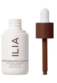ILIA Super Serum Skin Tint SPF 30 i en vit flaska med brunt text, har en pipettkork med bruna accenter och en vit bulb. 30 ml.
