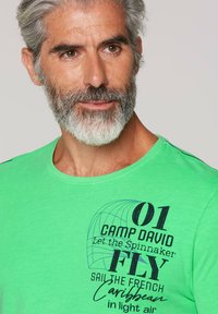 T-shirt verde in cotone con collo rotondo, maniche corte e stampa grafica con testo in vari caratteri e stili.