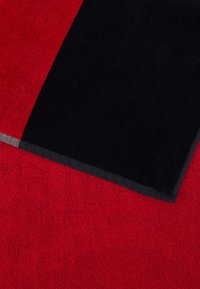 Κόκκινη και μαύρη πετσέτα με υφή στην επιφάνεια. Διαθέτει μια ενιαία κόκκινη περιοχή και ένα μαύρο τμήμα με ομαλή άκρη. Λεπτό μαύρο περίγραμμα στη ραφή.