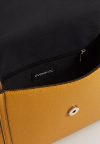 Žlutá kožená kabelka s texturou, černou textilní podšívkou, vnitřní kapsou na zip a stříbrným magnetickým uzávěrem.