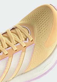 Hellgelber Laufschuh mit strukturiertem Mesh-Obermaterial, weißen Akzenten, lila Details und einer flexiblen Sohle mit "DREAMSTRIKE"-Markierung.