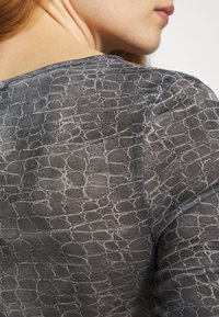 Durchsichtige schwarze Bluse mit einem strukturierten, rissigen Muster. Verfügt über einen runden Halsausschnitt und dezente Nähte entlang der Kanten. Leichtes, atmungsaktives Material.