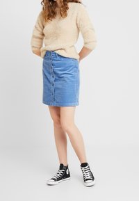 Jeanskjol med knappar i ljusblått, med vertikal ribbing, i kombination med en beige fluffig tröja och svarta högstövlar.