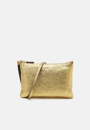 Petit sac bandoulière en cuir texturé doré avec une fine sangle et une fermeture éclair sur le dessus sur fond clair uni.