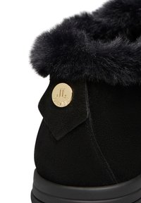 Stivale alla caviglia in suede nero con un morbido collarino in pelliccia nera e dettagli hardware con logo dorato. La suola è texturizzata e imbottita per garantire comfort.