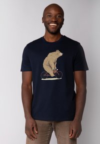 T-shirt en coton bleu marine avec une illustration d'ours faisant du vélo en beige et blanc, avec un col rond classique et des manches courtes.