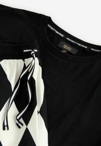 Čierne tričko a čierno-biele šortky so vzorom kosoštvorcov. Tričko má okrúhly výstrih; šortky majú elastický pás so sťahovacou šnúrkou.