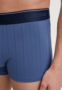 Navy blue cotton boxer shorts with vertical ribbed texture and a matching waistband featuring embossed "CALIDA" branding.